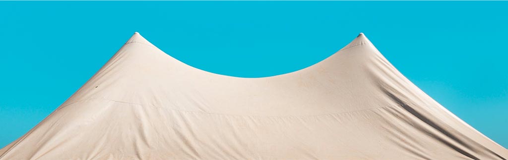 The peaks of a white event tent against a blue sky background